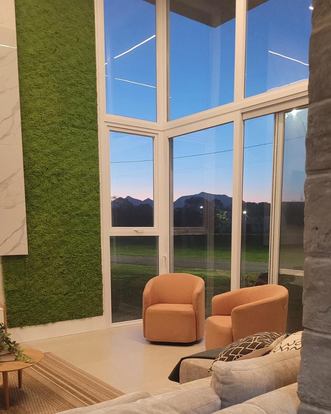 Living com jardim vertical, grandes esquadrias e vista para a serra ao entardecer